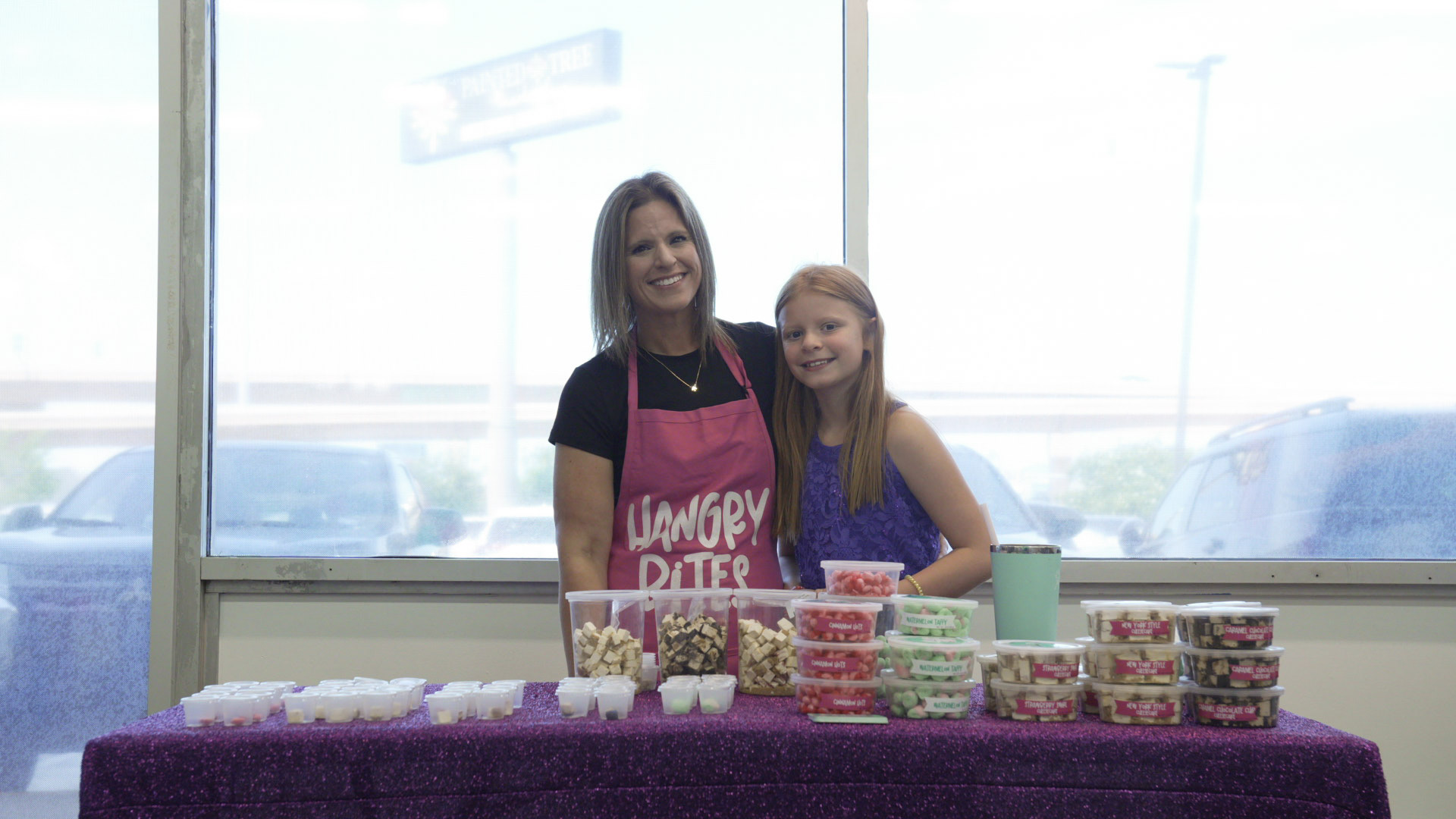 Vendor and her daughter smiling behind a table of treats at their Hangry Bites booth