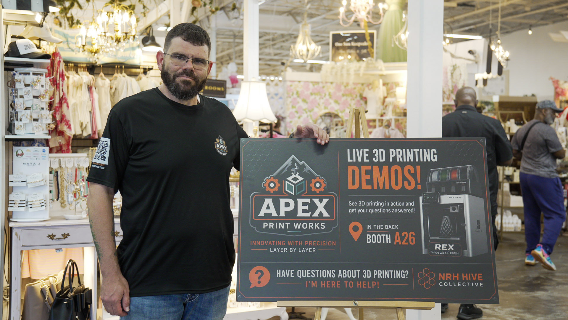 Vendor standing with an Apex Print Works 3D printing demos sign at NRH Hive Collective